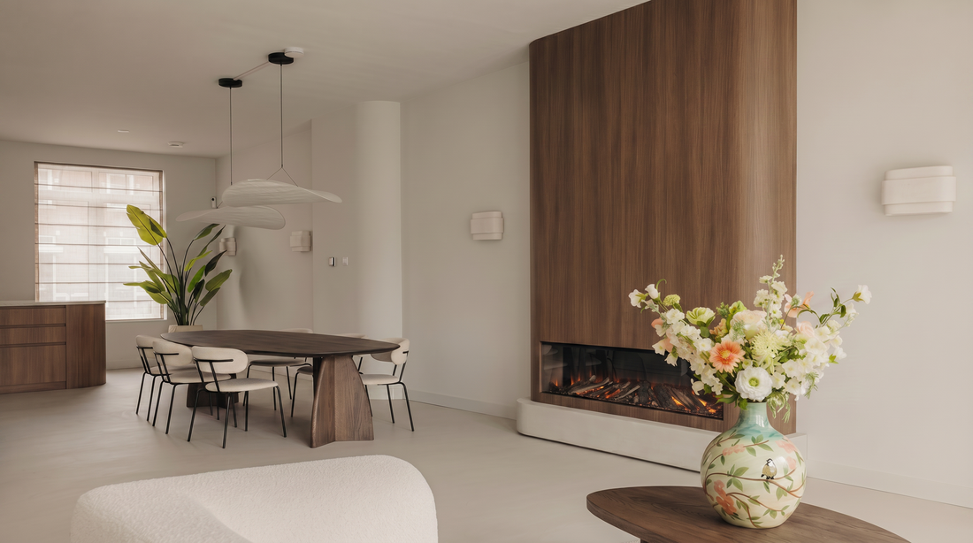 Japandi woonkamer met houten haardwand, eettafel en een boeket witte bloemen in een beschilderde keramieken vaas op een ronde salontafe