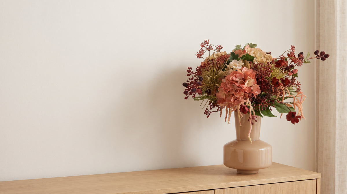 Kunstboeket met koraalkleurige hortensia in een beige vaas op een eiken dressoir in een lichte woonkamer